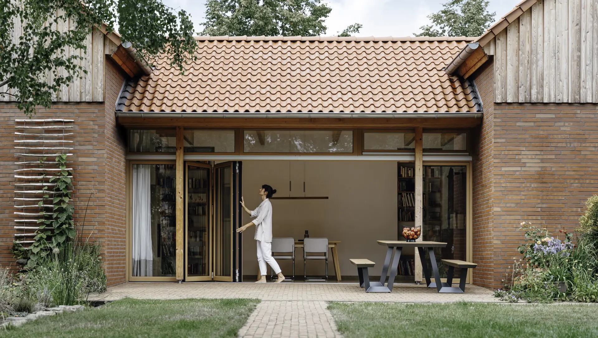 Frau öffnet Glas-Faltwand mit Holzrahmen.